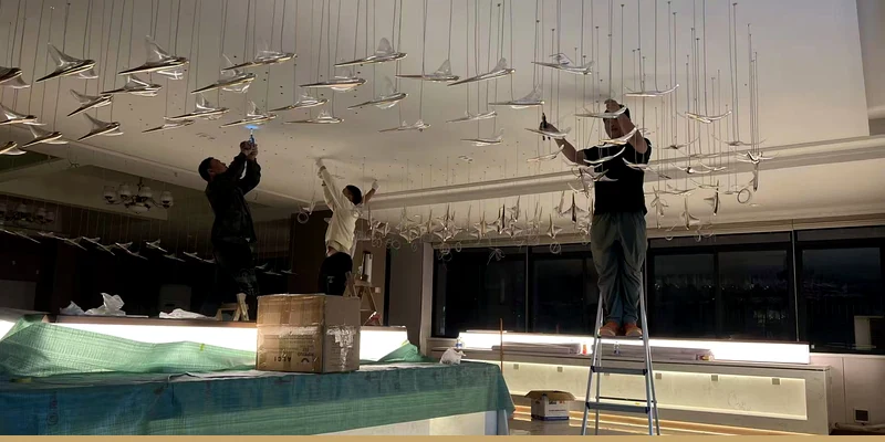 Cuslux installers positioning a hotel staircase chandelier made from individual suspended units Cuslux installers positioning a hotel staircase chandelier made from individual suspended units